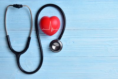Red heart with stethoscope on blue wooden background - representing healthcare