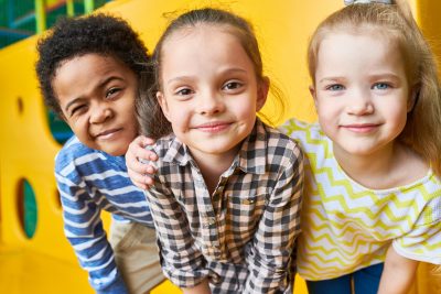 Colorful portrait of three happy kids posing looking at camera while having fun playing in children center