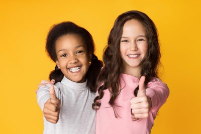 Two diverse girls smile and give a thumbs up