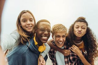 Close up of four happy teenage friends taking selfie outdoors. Girls piggy riding on the boys while taking a selfie outdoors.
