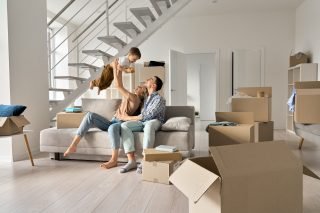 Happy young family couple playing with small toddler kid son together in new home. Parents and child boy having fun in new house living room with boxes. Moving day, mortgage, relocation concept