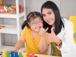 Portraits of a beautiful Asian teacher and a cute girl with autism doing an activity in a class. A child with a disability thumbs up and smiles to look at the camera.