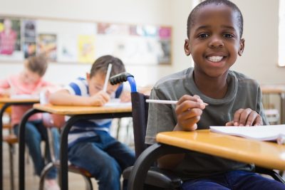 Child with a wheelchair smiling at camera in classroom