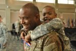 Male service member carrying a young boy piggyback, both smiling